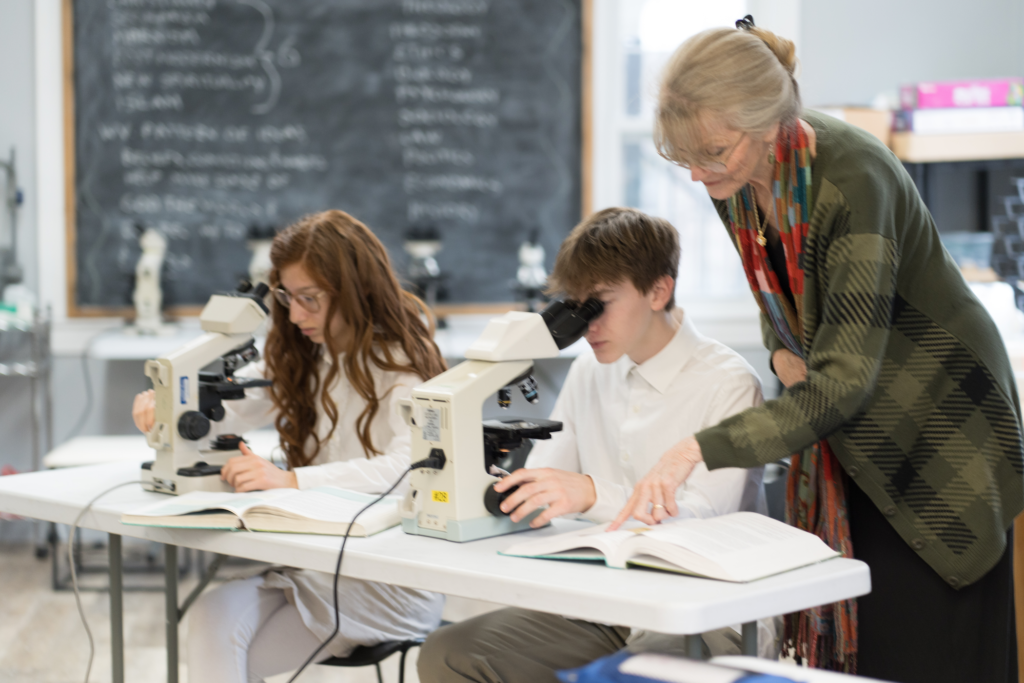 Mrs. Rose works with students in the Biology class using microscopes.